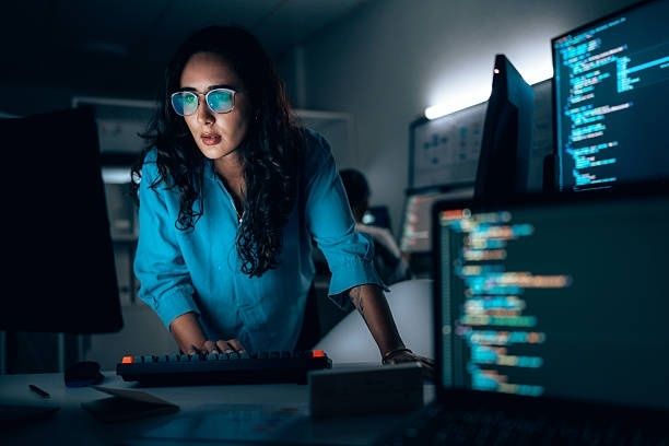 Person arbetar vid tangentbord framför skärmar med programmeringskod